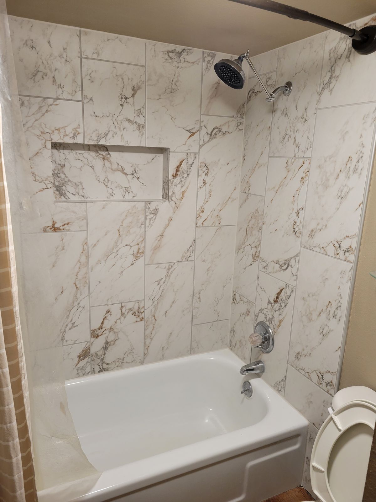 Completed tub-and-shower surround with large-format marble-look tile, a recessed niche, chrome showerhead and tub faucet, and a white tub.