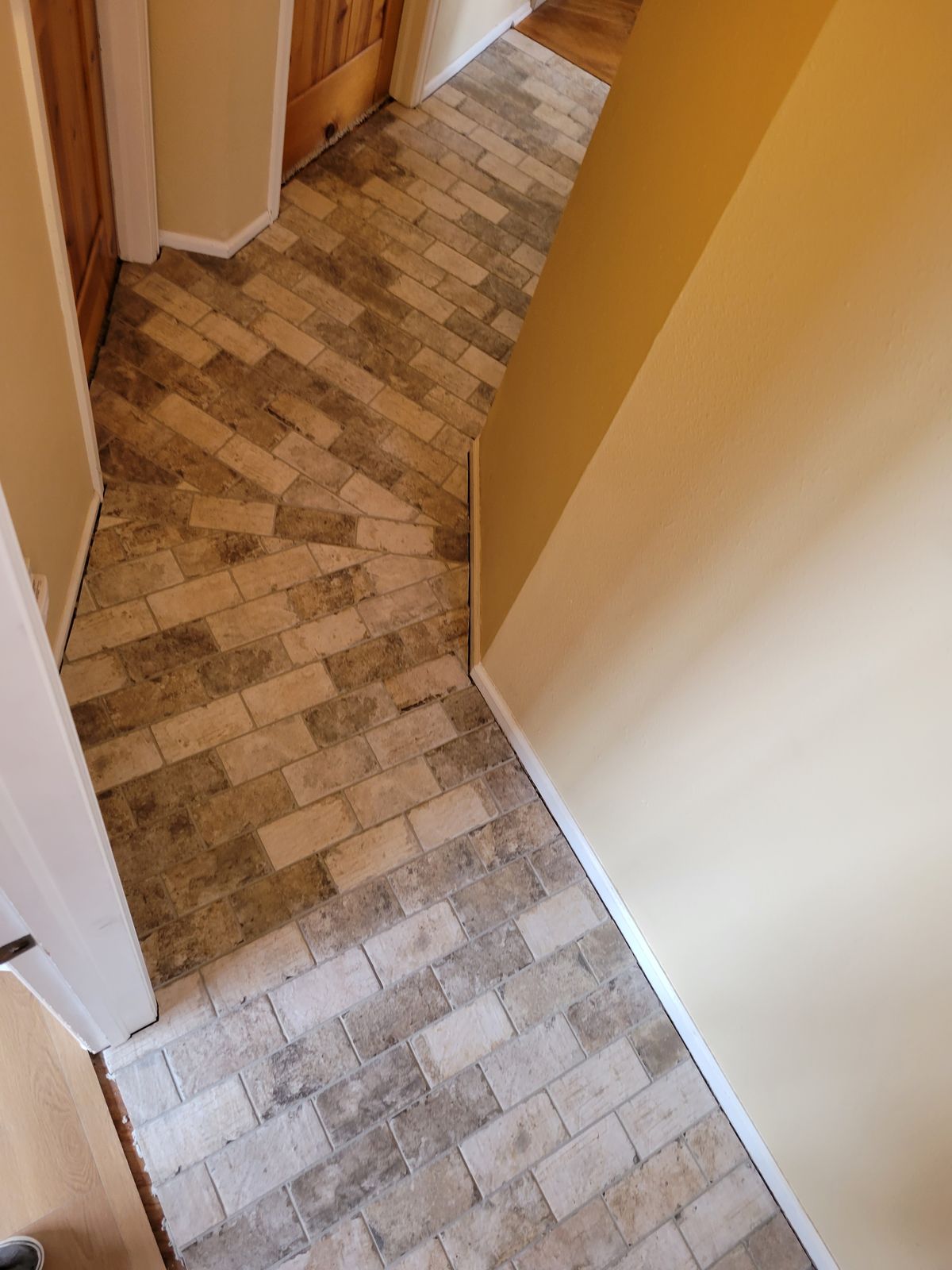 Hallway with completed diagonal brick-pattern tile flooring meeting a doorway, shot from above at an angle.