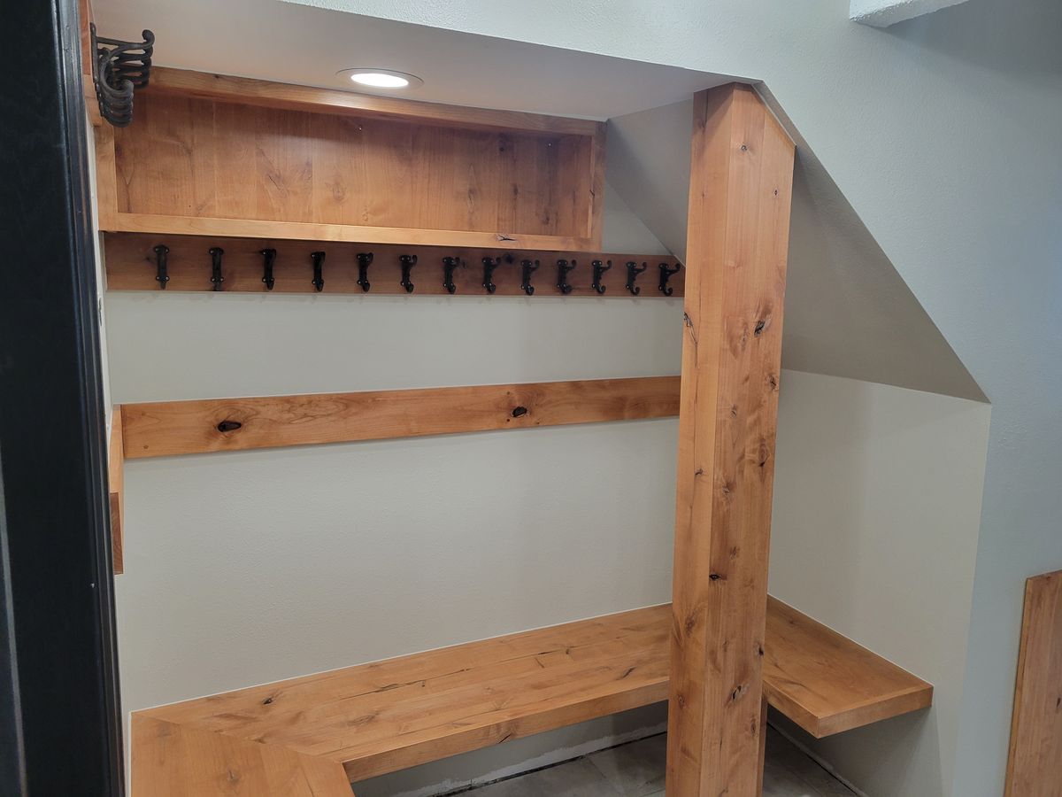 Close-up of the mudroom built-in showing a row of cast-iron coat hooks beneath a wood shelf with recessed lighting, flanked by a natural wood post and bench.